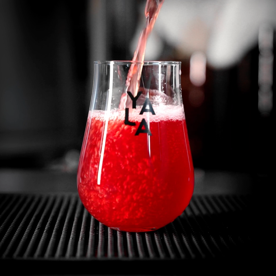 Red drink being poured into a glass with 'YALA' branding on a blurred background