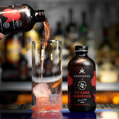 Hakkasan Lychee Hibiscus bottle being poured into a glass with ice, blurred bar background