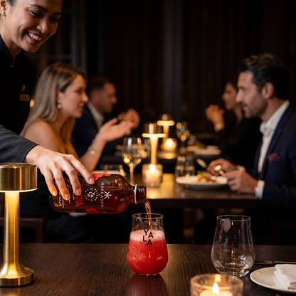Person pouring a drink into a glass with 'YALA' branding at a social gathering.